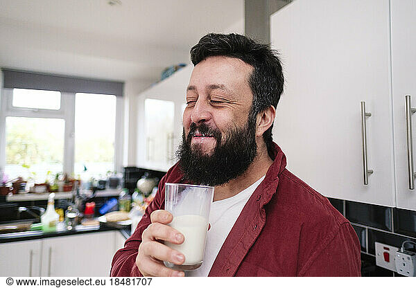 Smiling man enjoying glass of milk in kitchen at home