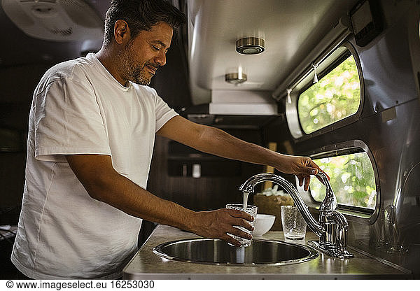 Smiling man filling drinking water through faucet in camper trailer