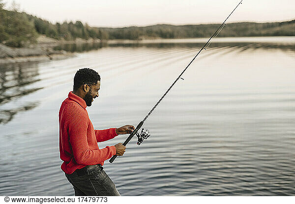 Smiling man fishing in lake during sunset