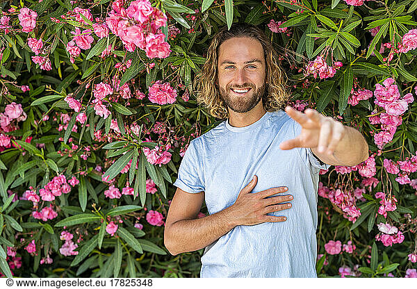 Smiling man gesturing in front of pink flowering plants