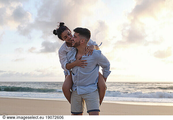 Smiling man giving piggyback ride to girlfriend at beach