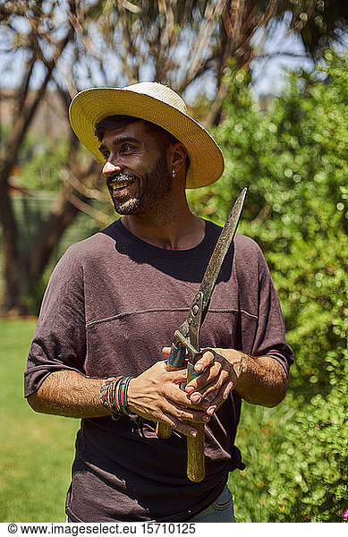 Smiling man holding a pruner in garden
