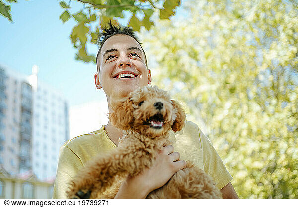 Smiling man holding dog near trees in park