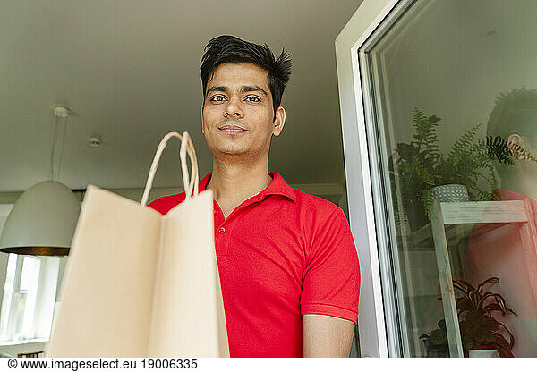 Smiling man holding grocery bag at home