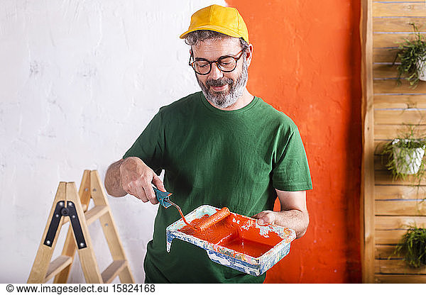 Smiling man holding paint tray with orange paint