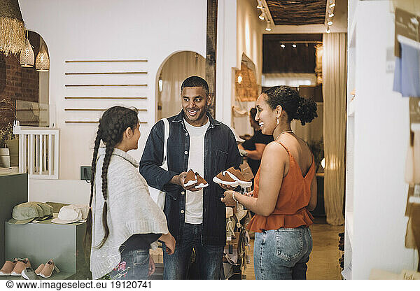 Smiling man holding shoes by daughter with saleswoman at boutique