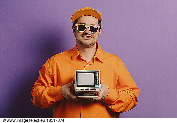 Smiling man holding vintage television set against purple background