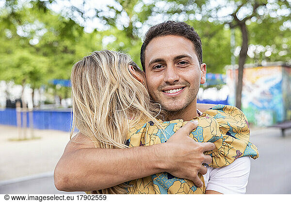 Smiling man hugging girlfriend at park