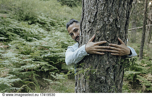 Smiling man hugging tree in forest