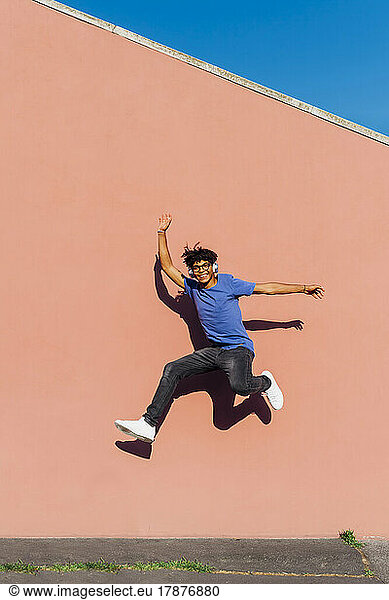 Smiling man jumping in front of wall on sunny day