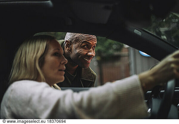 Smiling man looking away while talking to woman sitting in car