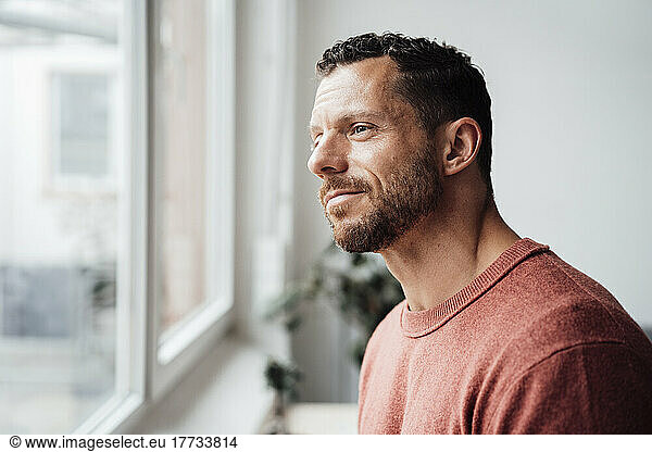 Smiling man looking out of window at home