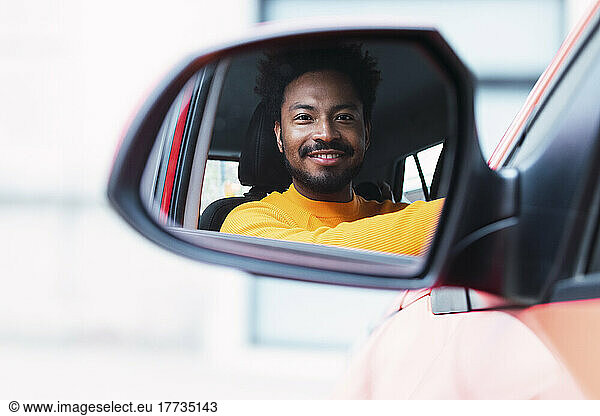 Smiling man looking through side-view mirror of car