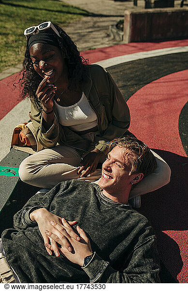 Smiling man lying on female friend's lap while relaxing in playground on sunny day