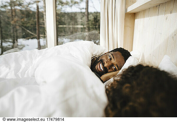 Smiling man lying with girlfriend on bed in cottage