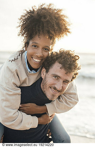Smiling man piggybacking girlfriend at beach