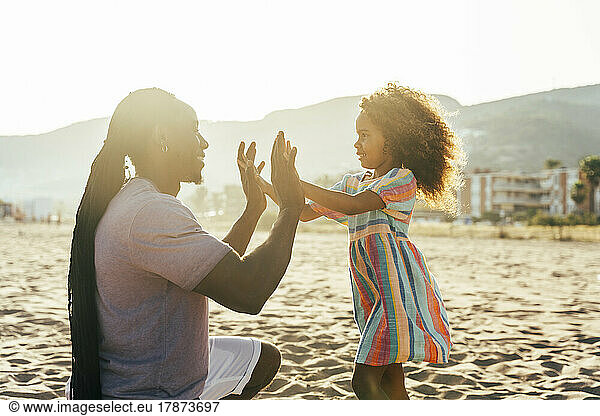 Smiling man playing clapping game with daughter at beach