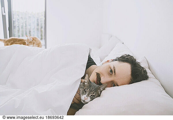 Smiling man relaxing on bed with cat at home