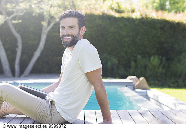 Smiling man relaxing on wooden deck by swimming pool