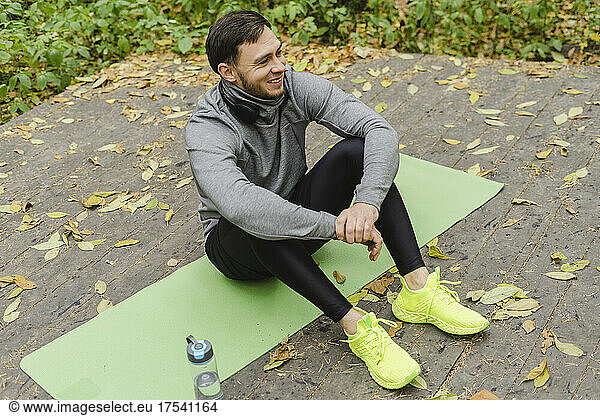 Smiling man resting on exercise mat at park