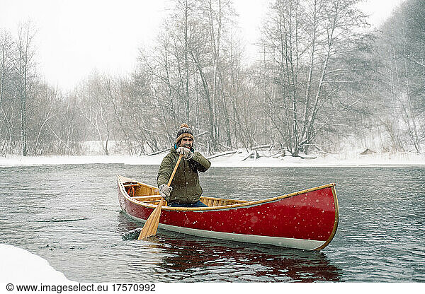 Smiling man riding red Canadian canoe in winter.