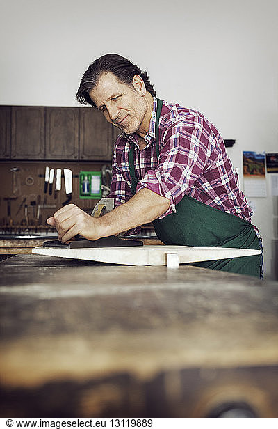 Smiling man sawing wood in workshop