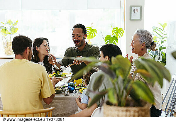 Smiling man serving salad to family at dining table at kitchen