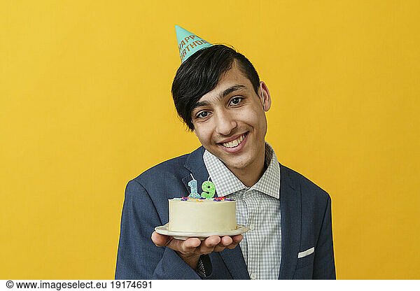 Smiling man showing birthday cake against yellow background