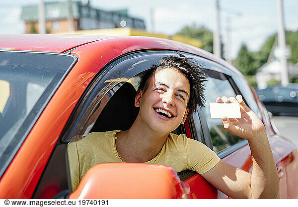 Smiling man showing driver's license and leaning out of car window
