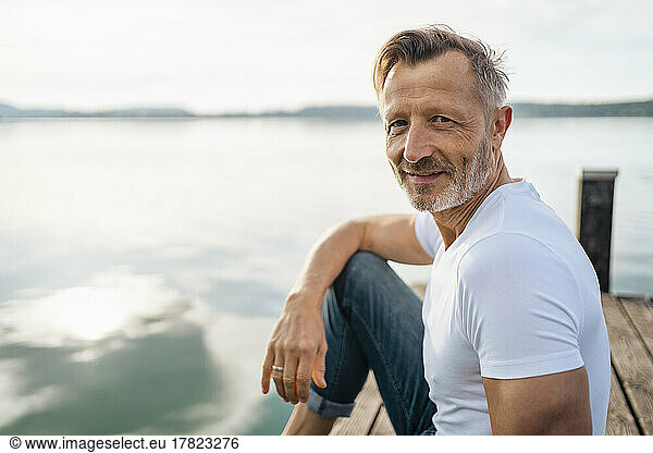 Smiling man sitting on jetty at lake