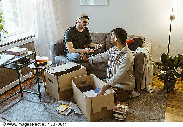 Smiling man sitting on sofa talking to boyfriend unboxing at home