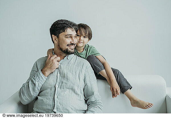 Smiling man sitting with son on white sofa