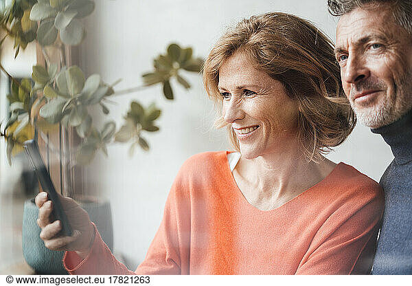 Smiling man standing by woman using smart phone in cafe