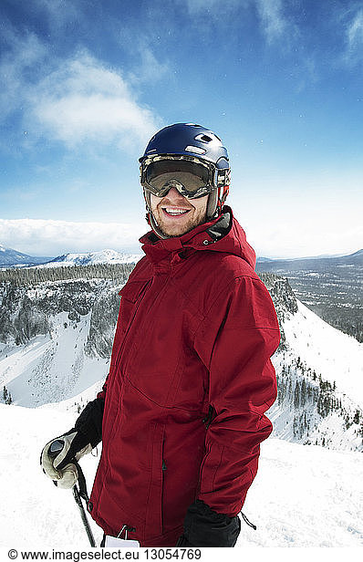 Smiling man standing on snowcapped mountain against sky