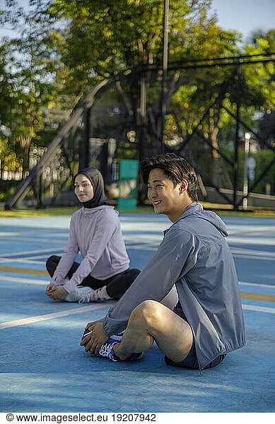 Smiling man stretching legs sitting on floor at sports court