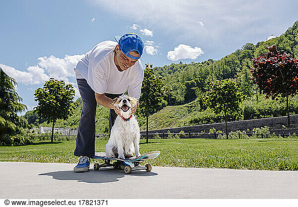 Smiling man stroking dog sitting on skateboard