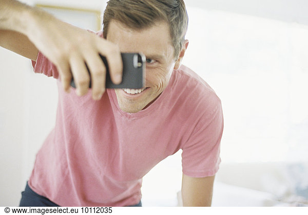 Smiling man taking a picture with a smart phone.