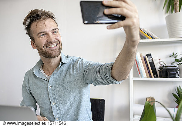 Smiling man taking a selfie at desk in office