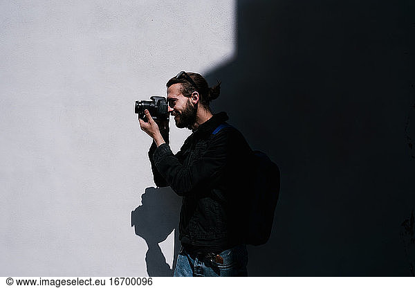 Smiling man taking pictures next to a black and white wall in the back