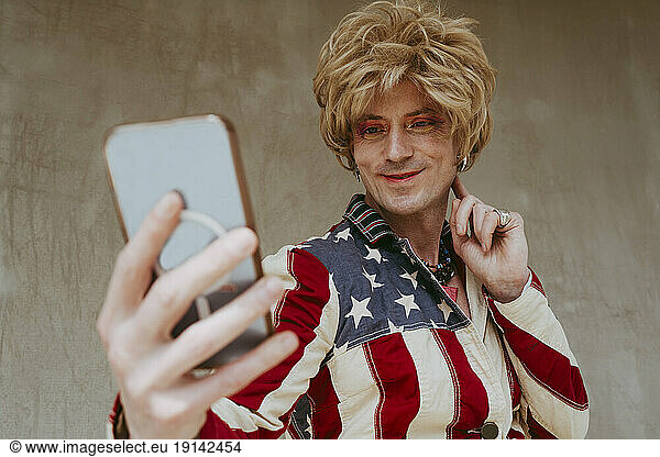 Smiling man taking selfie in front of wall