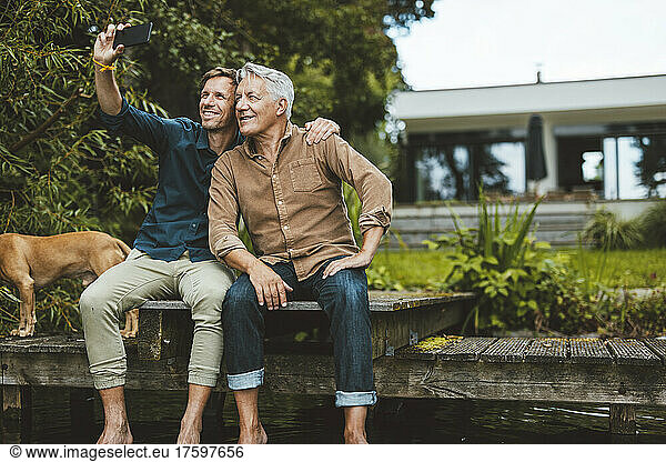 Smiling man taking selfie with father through smart phone at backyard