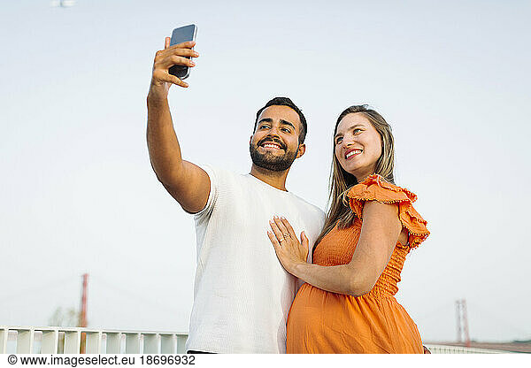 Smiling man taking selfie with pregnant woman