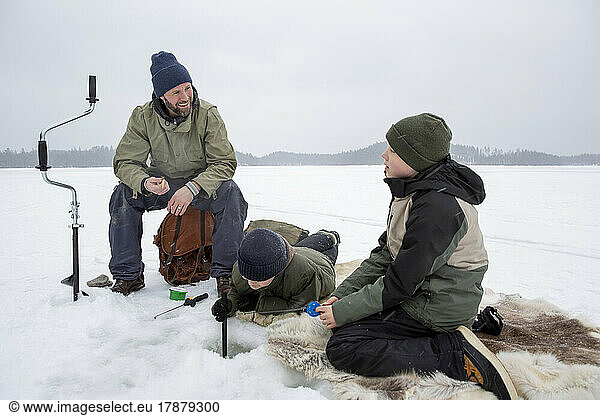 Smiling man talking with boy while son doing ice fishing at frozen lake