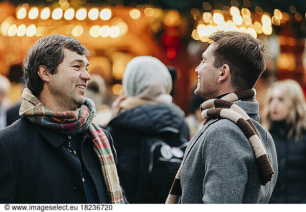Smiling man talking with father standing at Christmas market