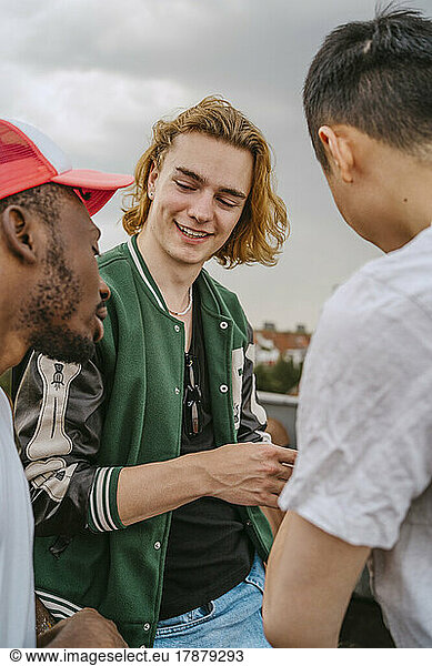 Smiling man talking with male friends against sky
