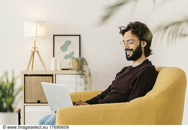 Smiling man using laptop sitting on sofa at home