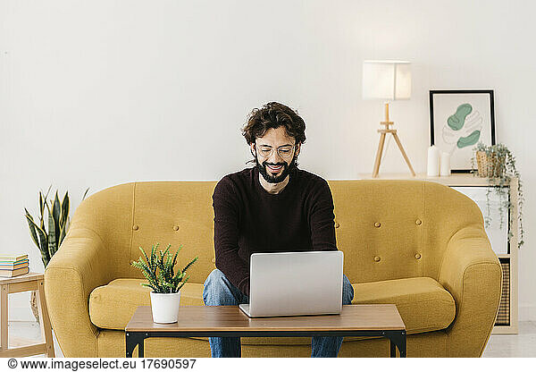 Smiling man using laptop sitting on sofa in living room at home