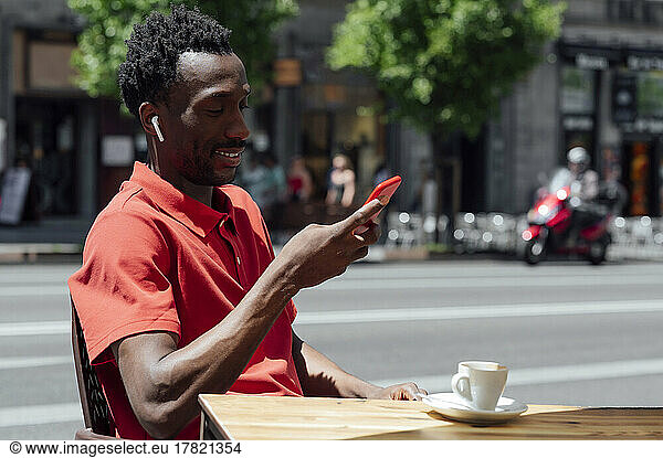Smiling man using mobile phone sitting at cafe