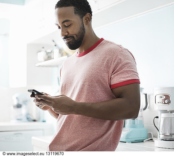 Smiling man using phone while standing at kitchen counter
