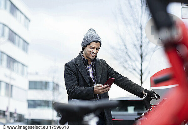 Smiling man using smart phone at bicycle parking station